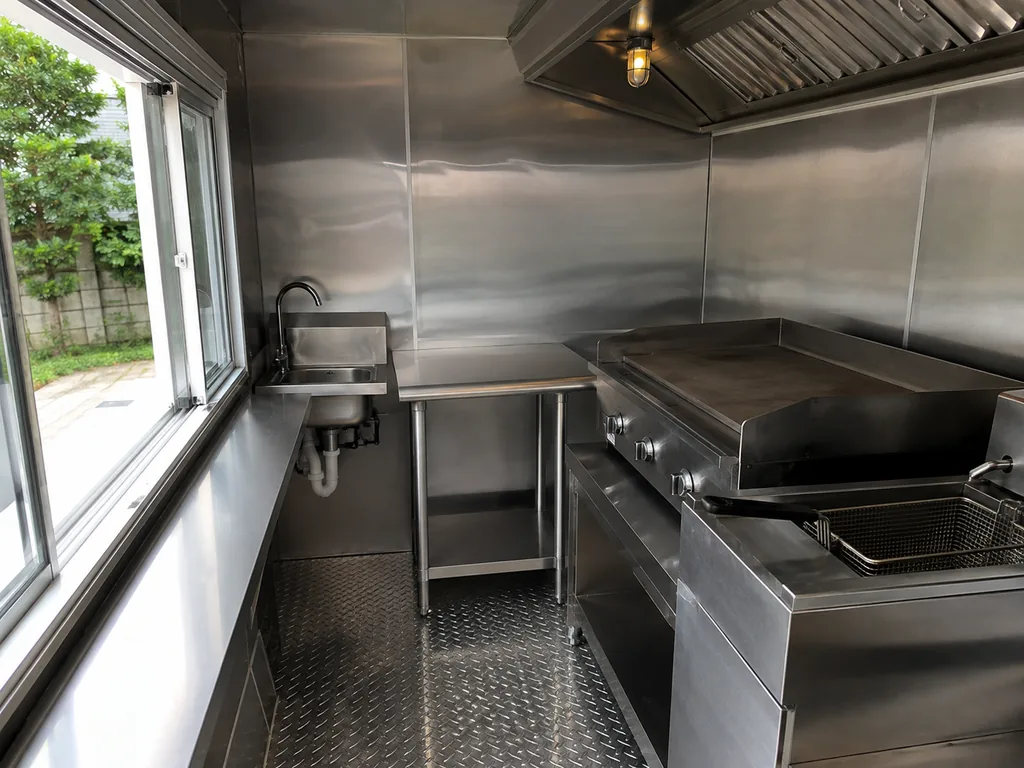 The inside of a food truck kitchen: a flat-top and fryer under a short hood, filters in the track.