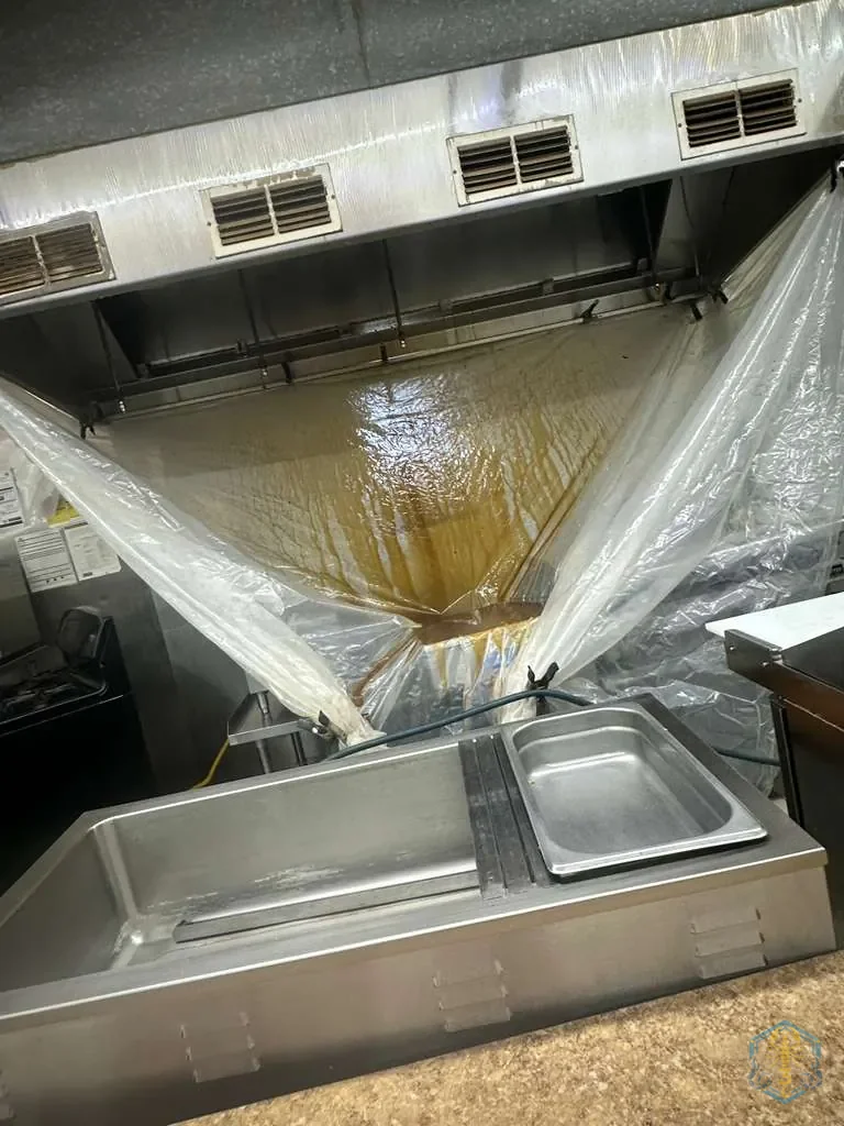 Plastic sheeting draped from the hood lip down into a collection pan, so wash water is contained instead of running onto the kitchen floor.