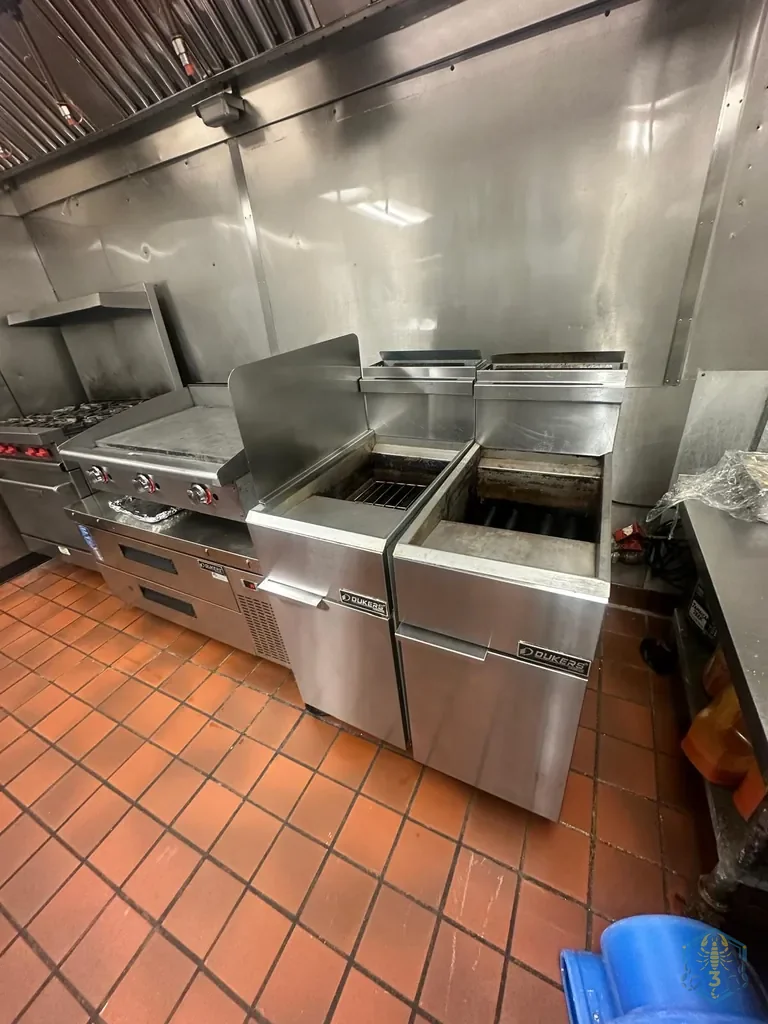 A restaurant cook line before cleaning: range, griddle, two fryers with greasy tops, and stainless wall panels with a grease film.