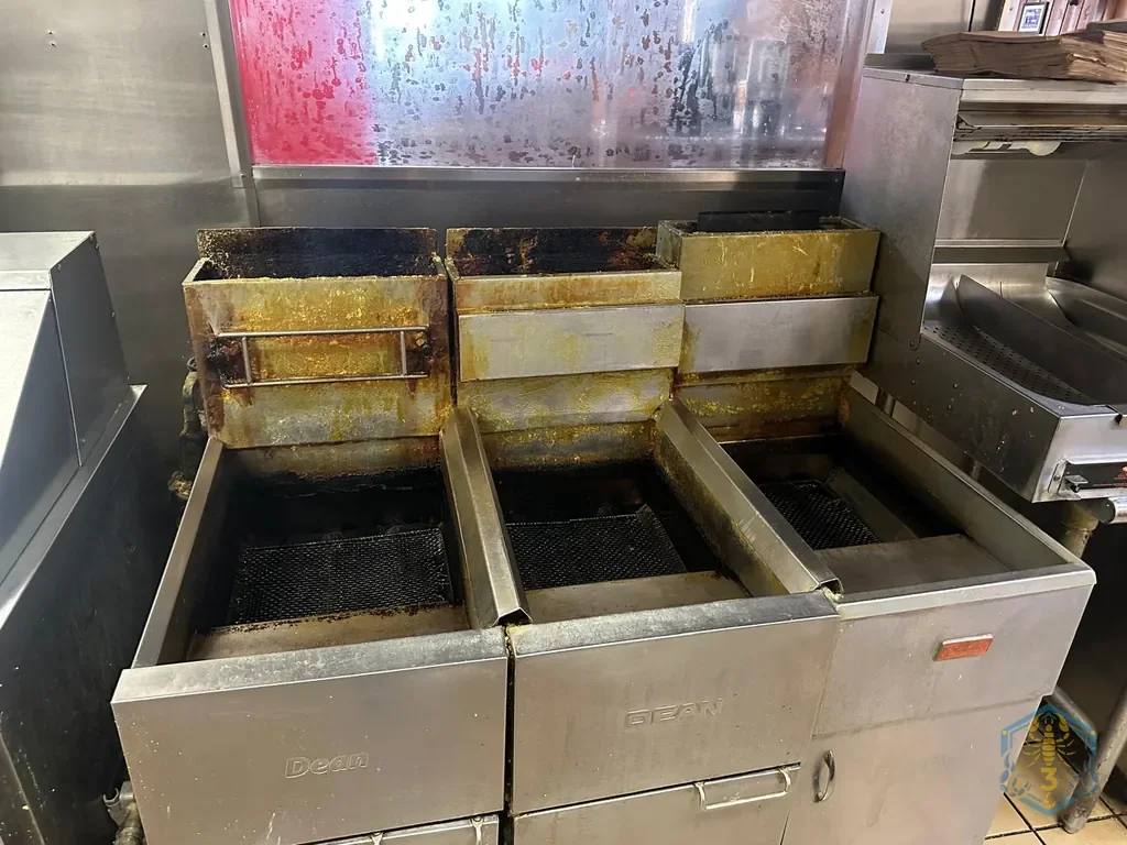 Three-vat fryer bank before cleaning: the rear decks are caked yellow-brown with old grease.