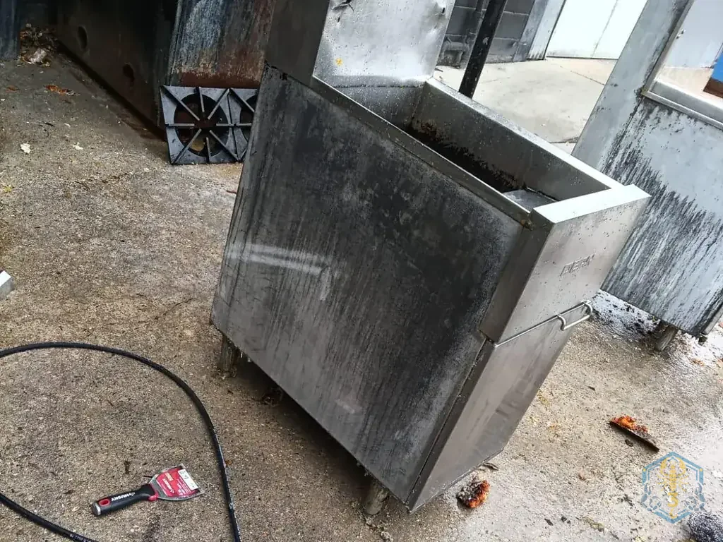 A fryer rolled outside to the back lot, being pressure-washed, hose on the concrete.